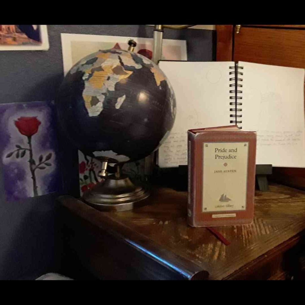 A little hardback copy of Pride and Prejudice sits on a wooden table next to a globe.