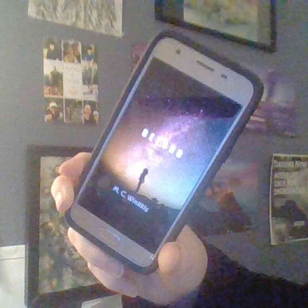 Beyond by M.C. Winkkle on a cell phone. On the cover: A girl in silhouette stands atop hills in front of a colorful starry sky.