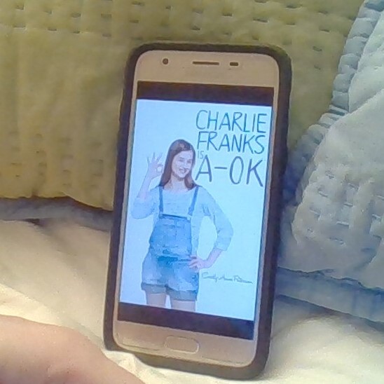 The cover of Charlie Franks is A-OK on a cell phone. A girl in overall shorts gives the OK sign.